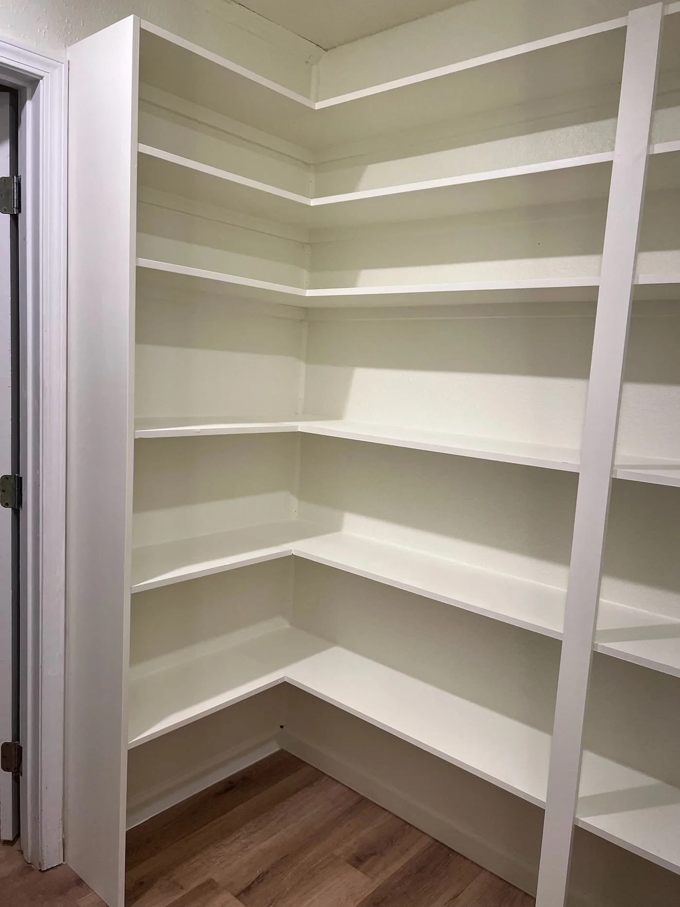 Newly built walk-in pantry with white wrap-around corner shelving