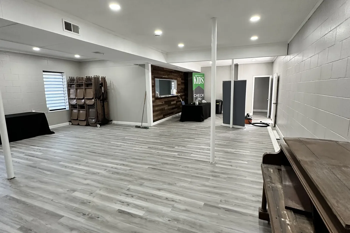 Renovated Greenville Community Church fellowship hall with new luxury-vinyl-plank flooring, a wood-accent feature wall, and a kids check-in area, completed by BHR Construction
