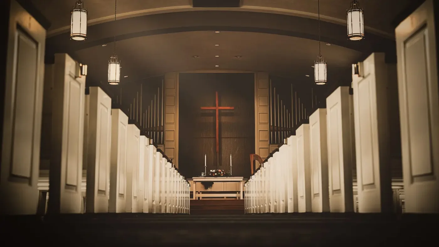 Church sanctuary interior with white pews, hanging lanterns, and a wooden cross above the altar