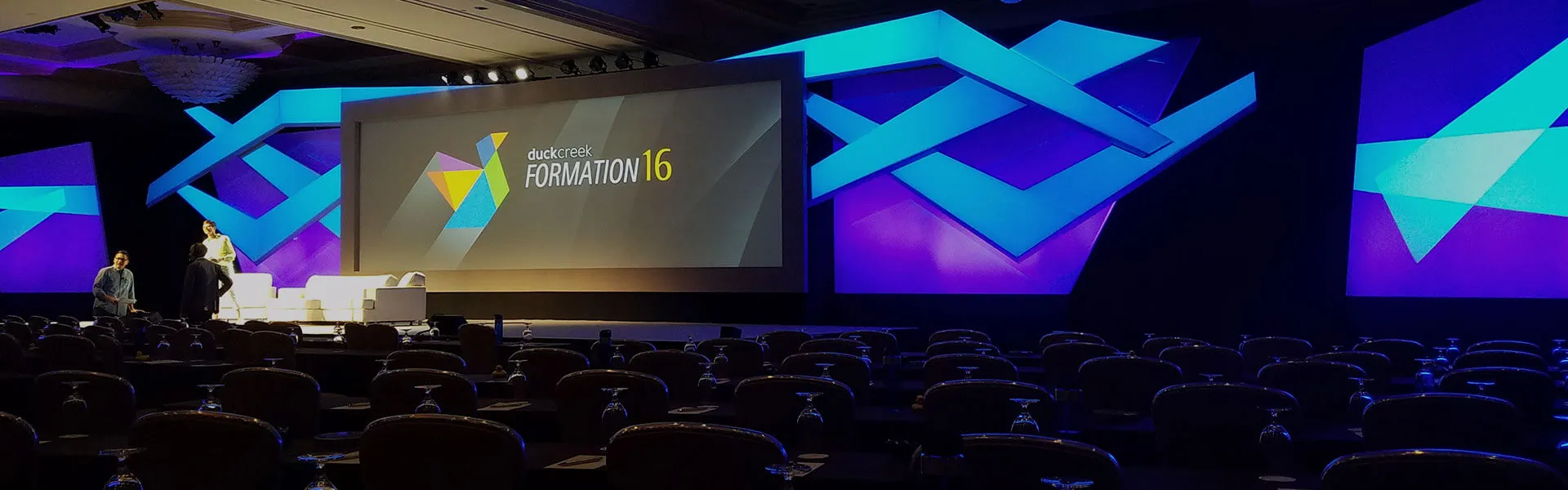 A branded conference stage set with LED screens and graphic scenic panels
