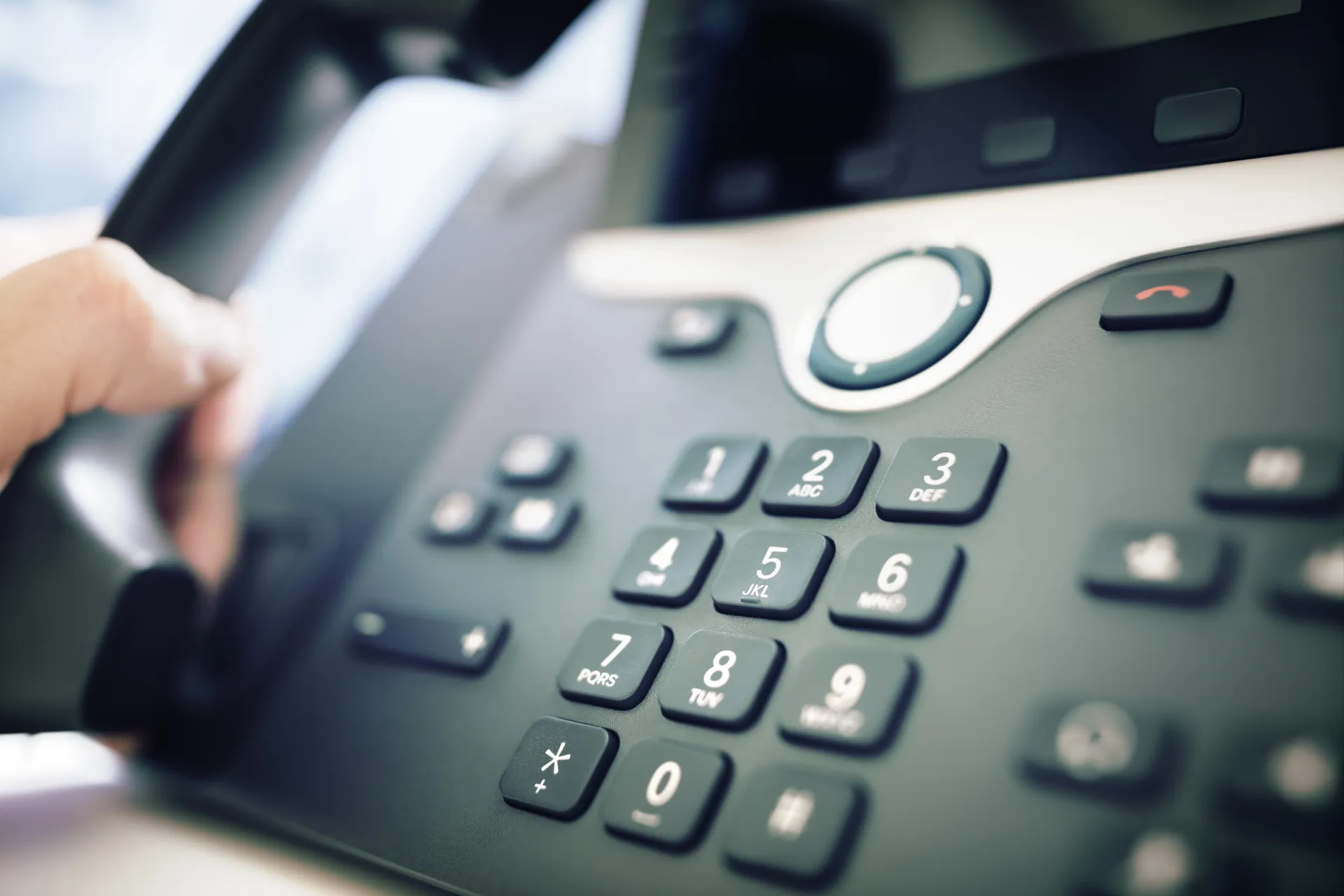 A hand dialing a desk telephone in an office