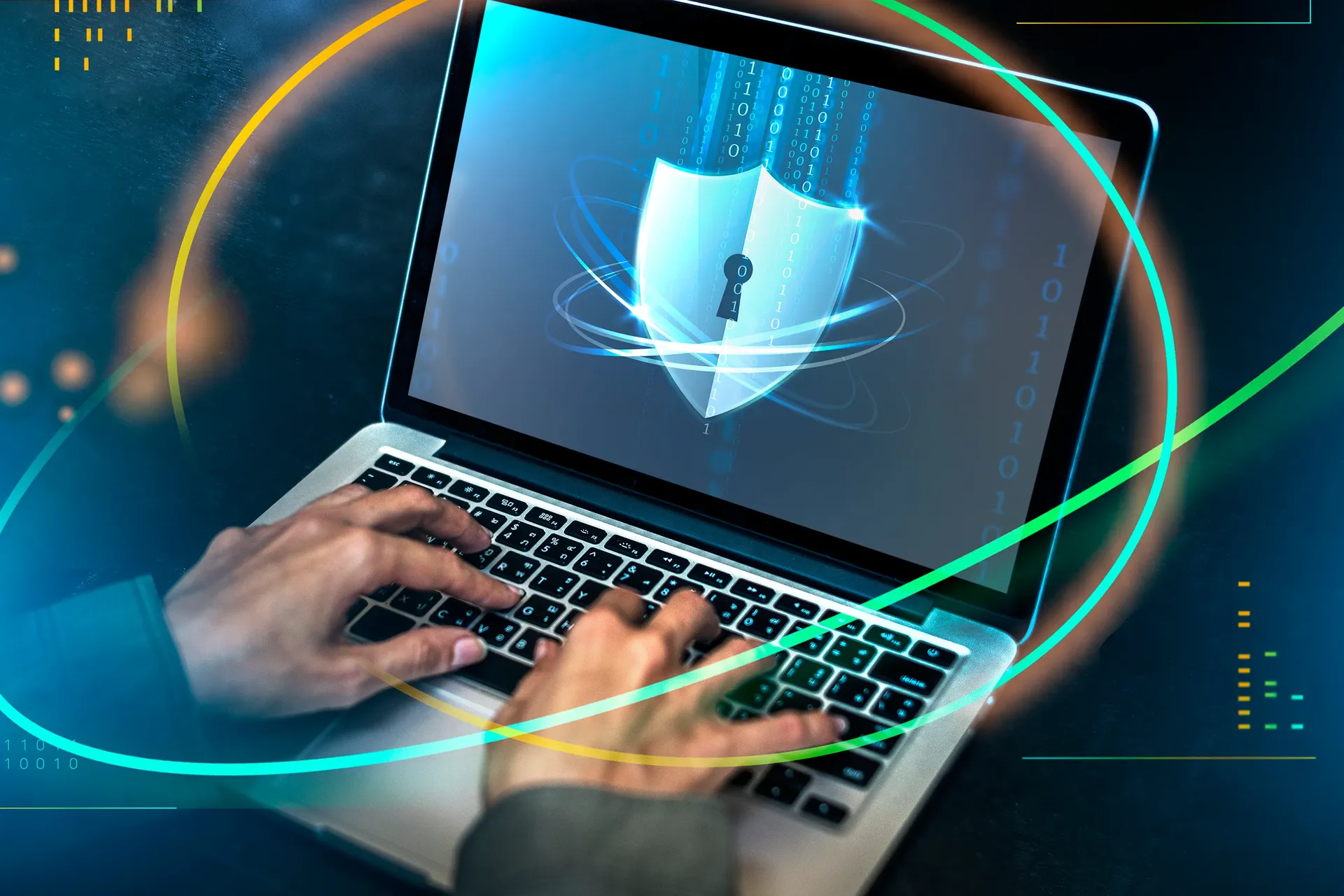 A hooded figure typing on a laptop in a darkened room