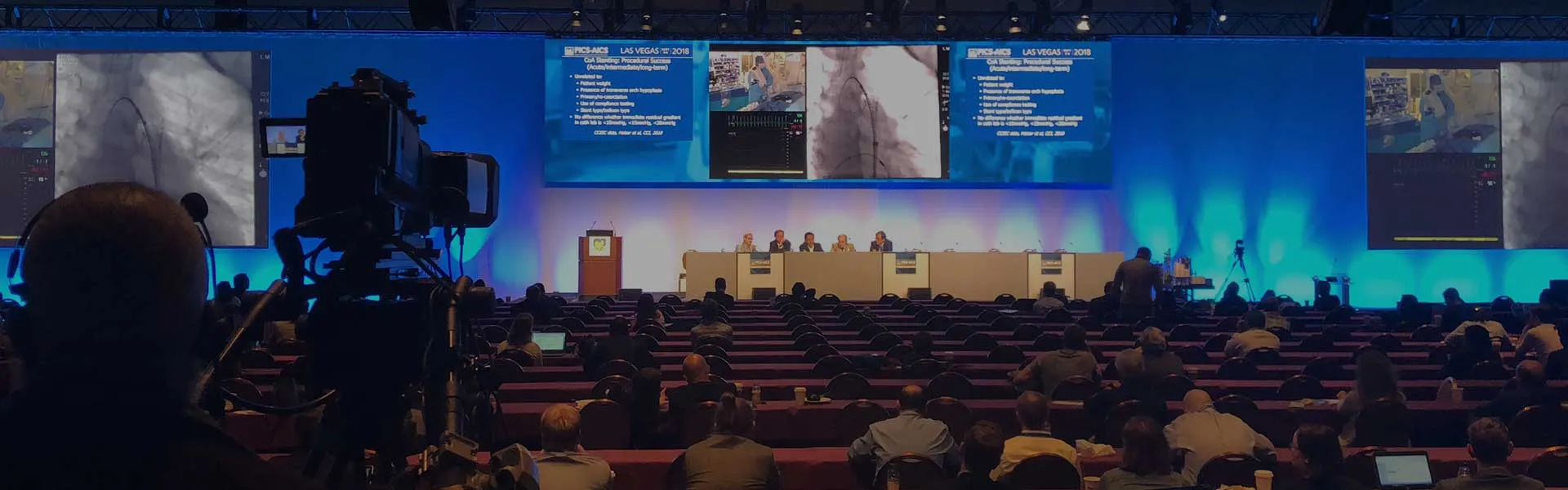 A panel stage with large screens in front of a full conference audience