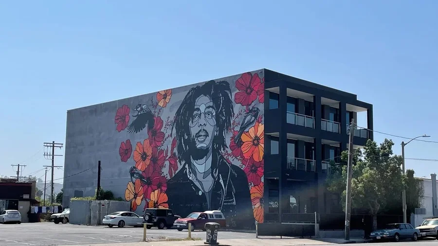 Large Bob Marley mural with red and orange flowers on a building in West Adams, Los Angeles