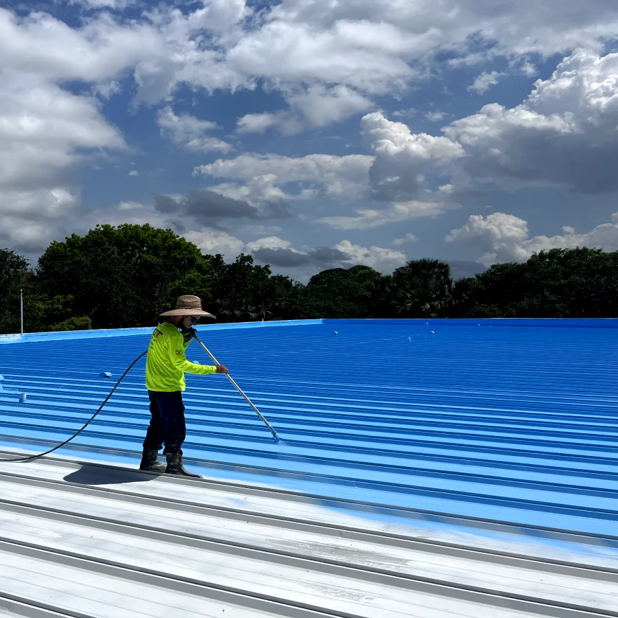 worker applying blue roof coating to a metal roof