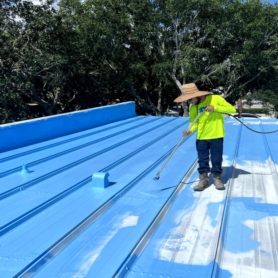 worker applying blue roof coating to a metal roof